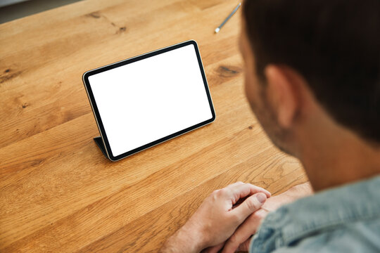 Man sitting at wooden table looking at tablet with blank screen
