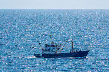 Fishing boat in blue sea and clear sky with birds flying overhead.