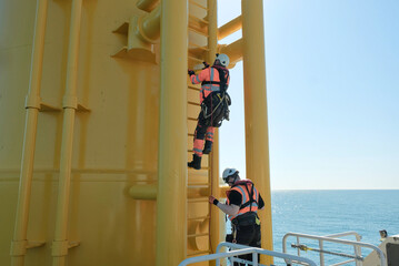Offshore Rigger Technician Climbing Yellow Wind Turbine Monopile Ladder During Wind Farm...