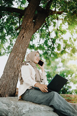 Fototapeta premium Photo of a Muslim student with a laptop by the sea. Working remotely by the beach. Happy and successful freelancer. Remote freelance work while on vacation.