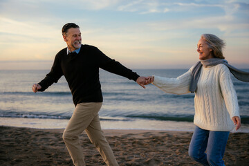 Cheerful mature couple holding hands and running at beach