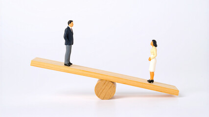 A wooden seesaw balancing a man and a woman figurine, representing a concept of balance