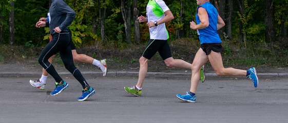 Four male runners running marathon in city park