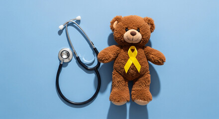 Teddy bear with yellow ribbon beside stethoscope on blue background. Banner template for childhood...