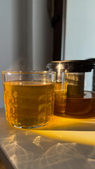 Golden sunlight caresses steaming herbal tea, evoking tranquil solace of International Tea Day and the meditative quiet of Hygge