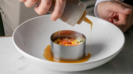 A culinary artist, European male, drizzles vibrant jus onto rainbow ceviche, celebrating International Chefs Day amidst metals and flavors