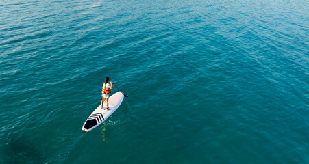Happy Asian woman  standing on a sup Surfing balancing on supboard paddling