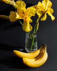 Golden iris blooms in crystal vase beside bananas, a sunny symphony celebrating Yellow Day,...