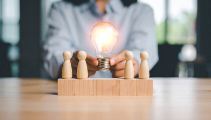 An illuminated light bulb held in front of four figurines representing teamwork and ideas