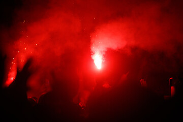 A crowd of people are gathered in a red smoke filled area