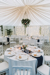 Wedding reception inside marquee with white draped ceiling, round tables and elegant floral decor