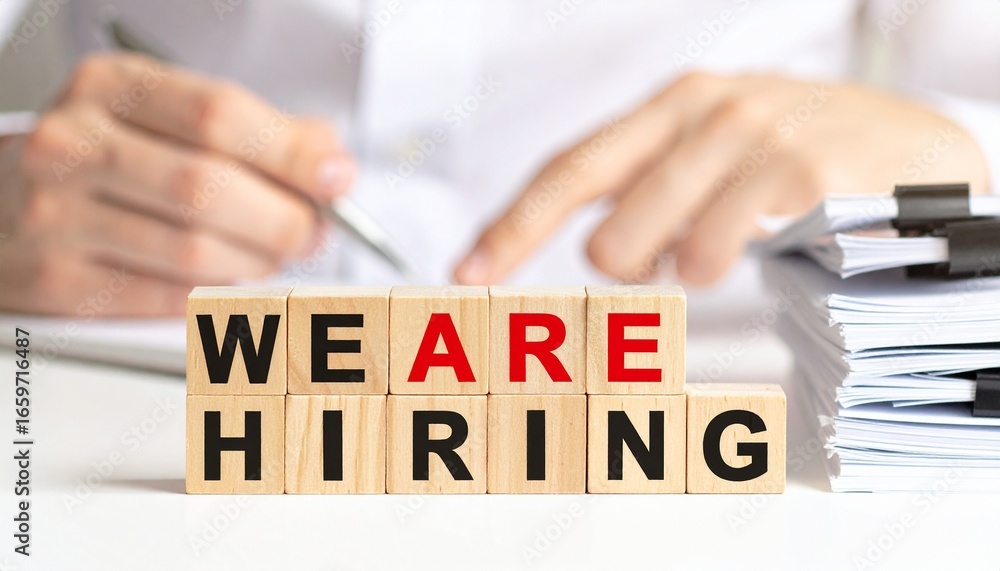 Poster wooden blocks with we are hiring in front of a person working in the office. the image captures the 