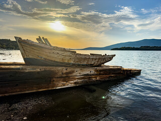 Weathered wooden fishing boat resting on pier at coastline during golden sunset with calm sea and...