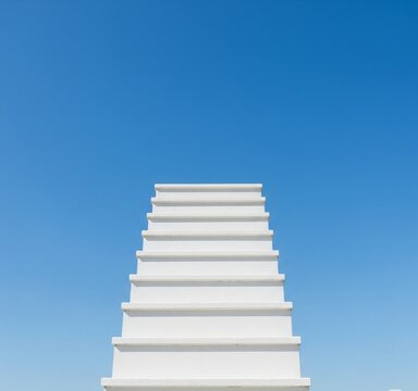 A minimalist, straight-on view of a clean white staircase ascending into a perfectly clear blue sky. This image symbolizes an unobstructed path to success, a new beginning, and progress. It is ideal 