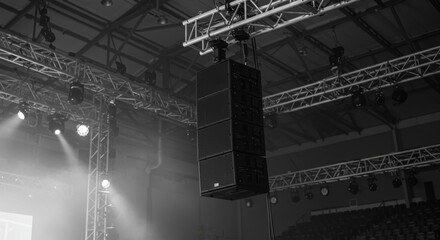 Monochrome Power - Professional Line Array Speaker Hanging from an Industrial Truss Amidst Hazy Stage Lights.