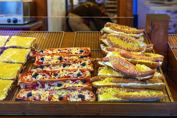 Hot sandwiches with melted cheese, sausages, pizza toppings displayed at festive food stall. Concept of Christmas cheese sandwich, quick meal, winter comfort street food