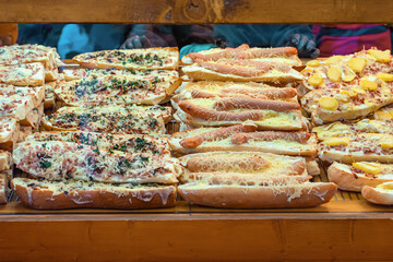 Freshly baked baguettes topped with sausages, cheese, herbs, and potatoes at food stall. Concept of...