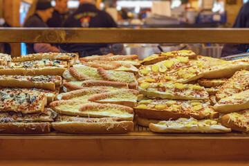 Baked baguettes filled with sausages, cheese, and toppings displayed at food stall. Concept of Christmas market, market food, holiday snacks, and street-style baking