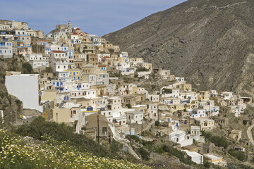 Greek village of Olympos, Karpathos island with whitewashed buildings, and a central clock tower. windmill stands in the background, with the Greek flag 