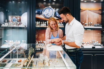 Elegant couple enjoying a moment in a jewelry store, trying on luxury watches while smiling and...