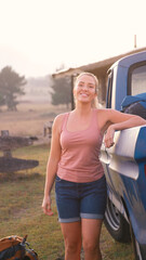 Portrait Of Young Woman Loading Backpack Into Pick Up Truck For Road Trip To Cabin In Countryside