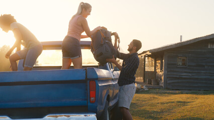 Group Of Friends Unloading Backpack From Pick Up Truck On Road Trip To Cabin In Countryside