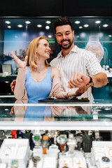 Elegant couple enjoying a moment in a jewelry store, trying on luxury watches while smiling and embracing, making a thoughtful purchase decision for a special occasion