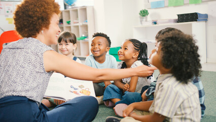 Female Teacher Reads And Asks Questions To Multi-Cultural Elementary School Pupils In Class