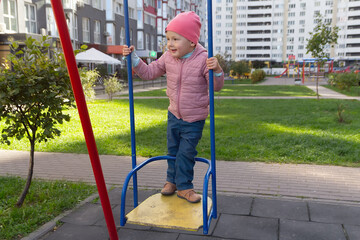 Cute baby on the swing on the playground near the house