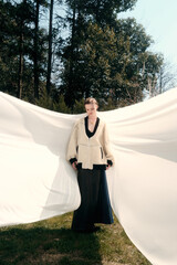 Woman in elegant outfit posed with flowing fabric outdoors.
