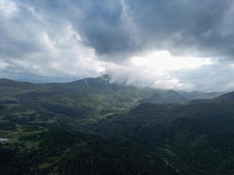 Aerial view of a majestic mountain peak partially veiled by ethereal clouds, rising above a verdant landscape of dense forests and winding valleys, Posof, Ardahan, T&Atilde;&frac14;rkiye.