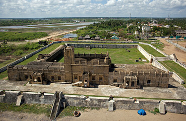 Aerial view of a historical fort stands with weathered stone against a backdrop of wetlands and distant buildings, Tharangambadi, Tamil Nadu, India.