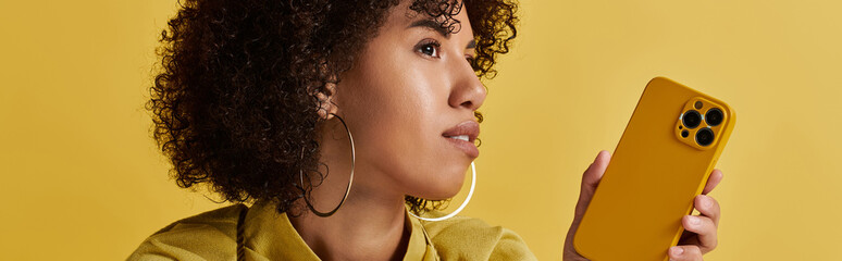 Curly woman showcases trendy yellow outfit and gadget in vibrant studio setting