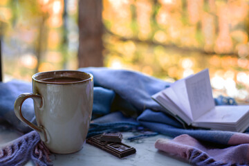 Tranquil autumn moment featuring warm cup of coffee, chocolate pieces, and an open book on table. For relaxation and introspection themes.