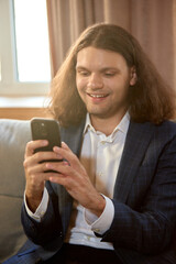 Young man in suit holding smartphone with cheerful smile. Concept of communication, technology,...