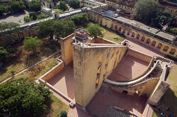 Aerial view of the Samrat Yantra, a colossal sundial, stands out with its stark geometric form against the surrounding greenery and historic architecture, Jaipur, Rajasthan, India.