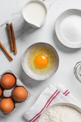 Baking ingredients flat lay with flour, eggs, sugar, and spices on marble surface