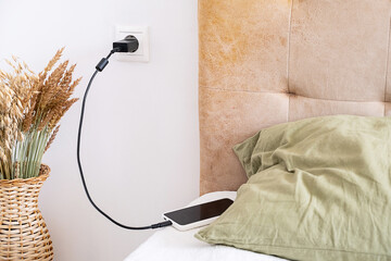 Phone charging cable connected to wall socket next to bed.