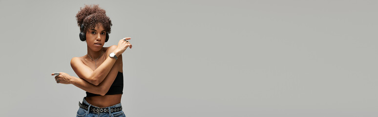 Curly African American woman expresses style in trendy outfit against grey backdrop