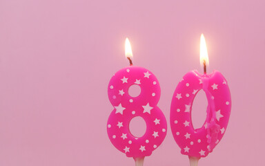 Pink birthday candles with stars burning on pink background, number 80.	