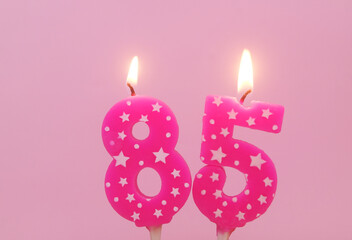 Pink birthday candles with stars burning on pink background, number 85.