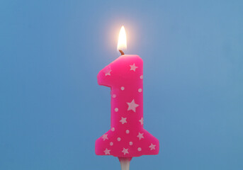 Burning pink birthday candle with white stars on blue background, number 1.	