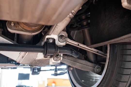 Car rear axel assembly with control arm, coil spring, shock absorber and stabilizer bar. Wide angle, looking up shot of a lifted car in a repair shot, no people