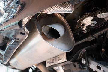 Car single exhaust muffler pipe and tip on a lifted car inside repair shop. Close up, wide angle,...