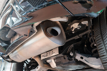 Car single exhaust muffler pipe and tip on a lifted car inside repair shop. Close up, wide angle,...