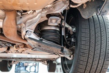Car rear axel assembly with control arm, air suspension shock absorber with rubber boot. Wide angle, looking up shot of a lifted car in a repair shot, no people