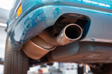 Car single exhaust muffler pipe and tip on a lifted car inside repair shop. Close up, wide angle,...