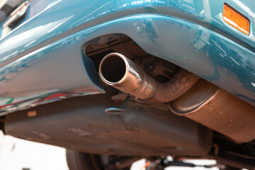Car single exhaust muffler pipe and tip on a lifted car inside repair shop. Close up, wide angle,...