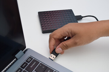 Hand plugging USB flash drive into laptop with external hard drive nearby, concept of data...