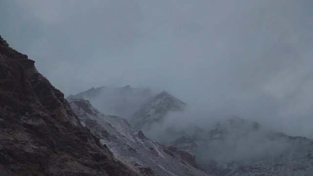 Dark clouds above the snowy Himalayan mountain peaks during a winter storm as seen from near Gonbo Rangjon mountain in Zanskar Valley, Ladakh, India. Slight snow on the mountain peaks due to storm.	